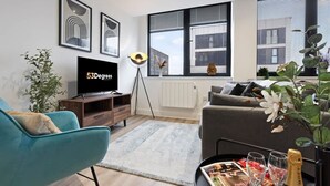 A modern living room with a flat-screen TV, a sofa, a coffee table with magazines and glasses, a floor lamp, and large windows with city views. - Pristine Flat Ideal for Small Groups Sleeps 4 (Manchester)