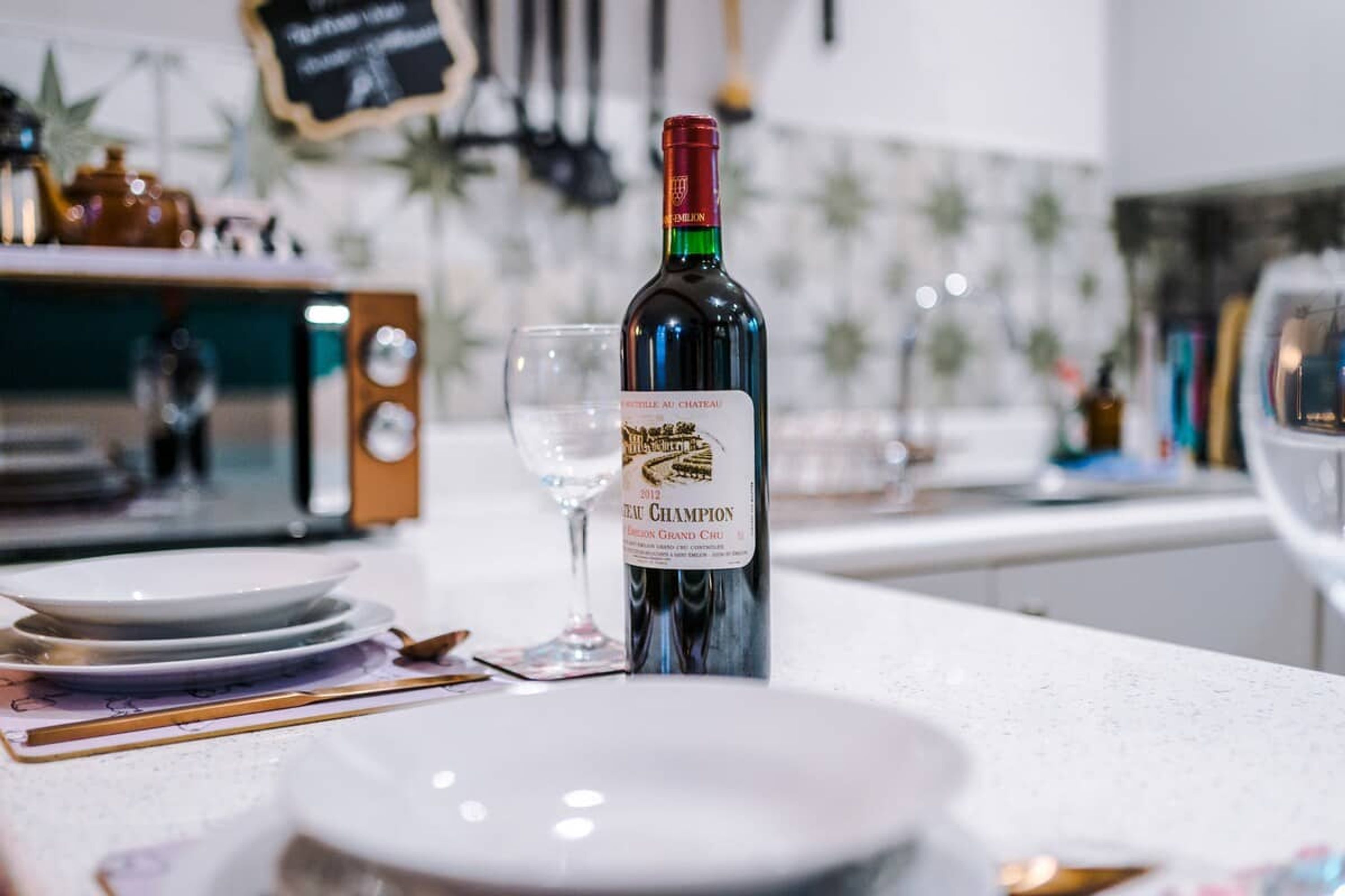 En flaske 2012 Chateau Le Grand Chru vin, et vinglas samt et borddække med tallerkener og bestik.