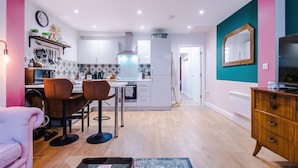 A modern kitchen with white cabinets, a central island, and a dining area with two chairs. - Stunning City Centre Home Perfect For Couples (Chester)