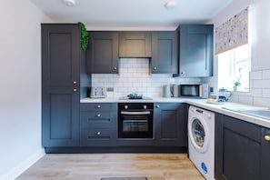 A modern kitchen with dark cabinetry, a built-in oven, a microwave, and a washing machine. - NEW Stunning Home Ideal for Groups Free Parking (Chester)