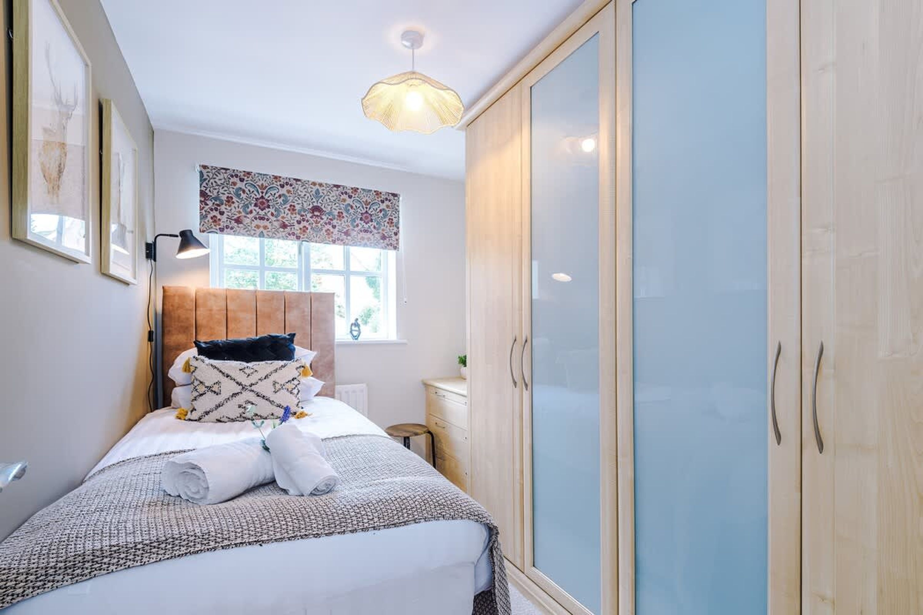 A bedroom with a bed, bedside table, lamp, window with curtains, and a wardrobe.