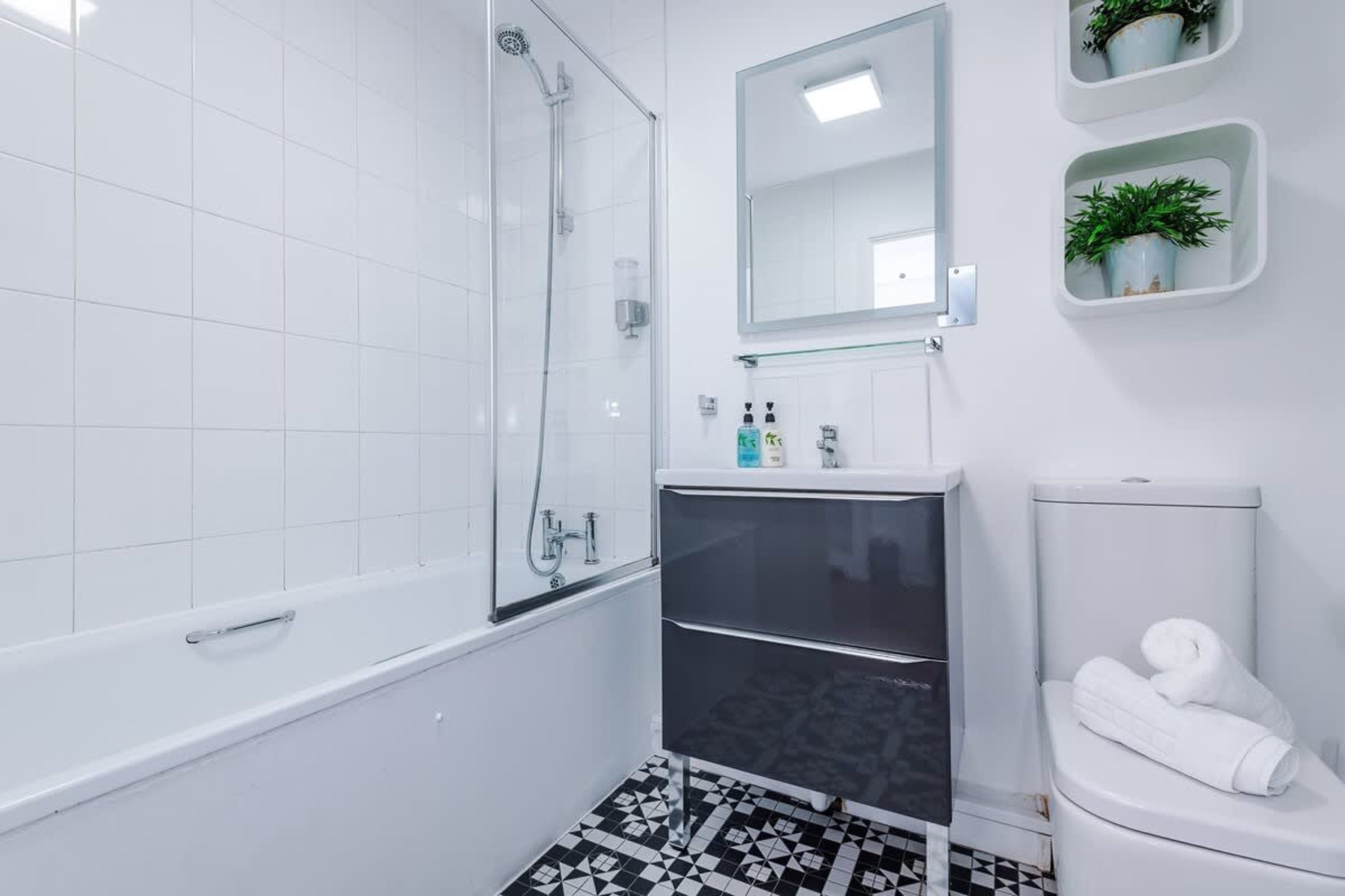 Un baño con bañera, ducha con mampara de vidrio, inodoro y lavamanos con espejo superior.
