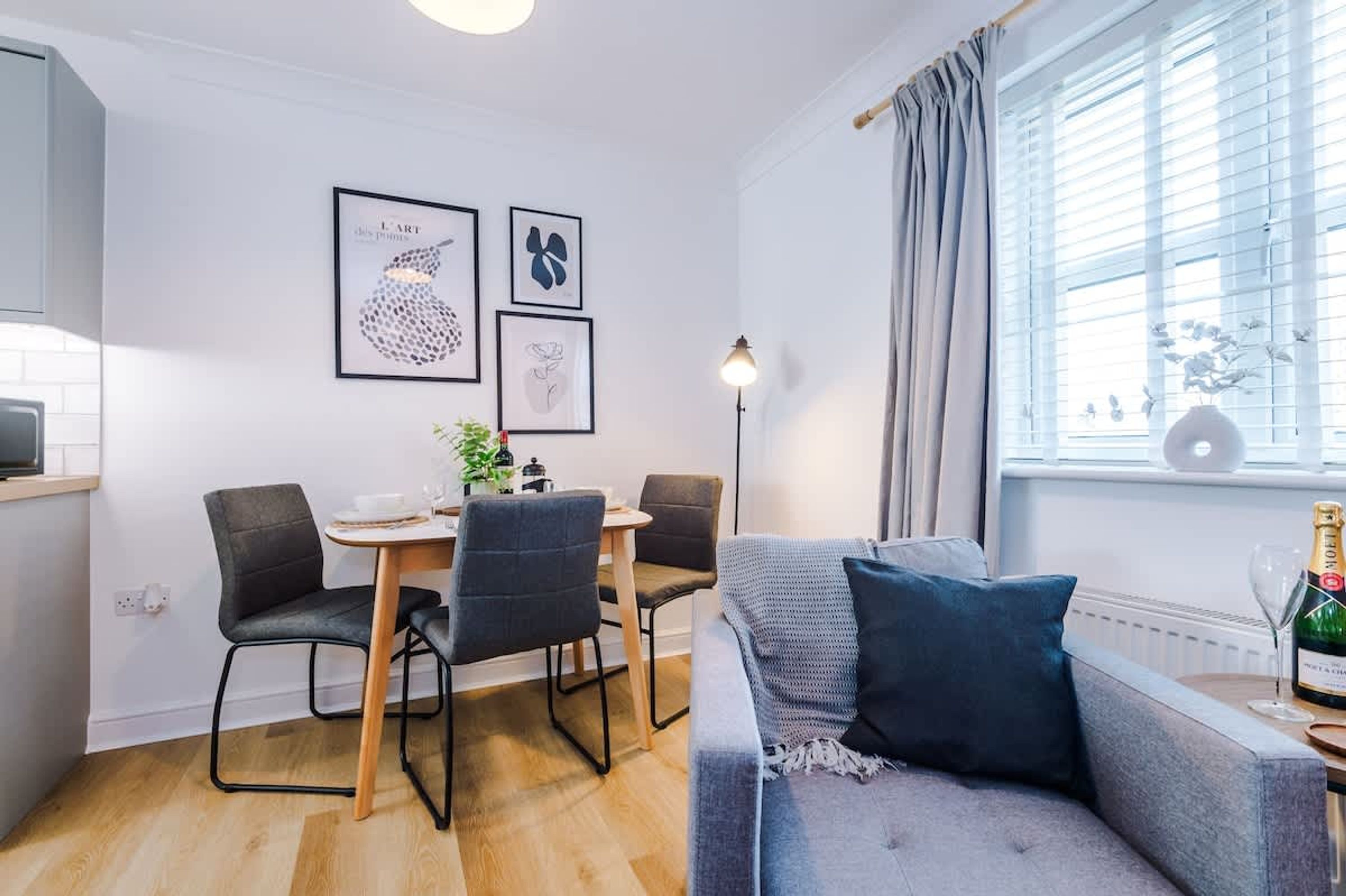 A modern living room with a grey sofa, a dining table with chairs, and a window with curtains.