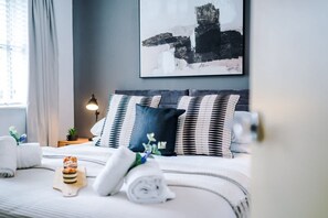 A neatly made bed with striped pillows, a rolled towel, and a small plant on a bedside table. - New Stunning Flat Perfect for Business Sleeps 3 (Crewe)