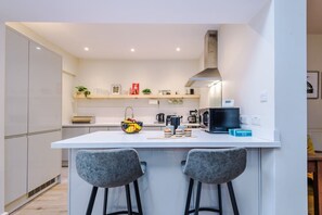 Cocina moderna con una isla central, dos taburetes de bar y varios electrodomésticos.