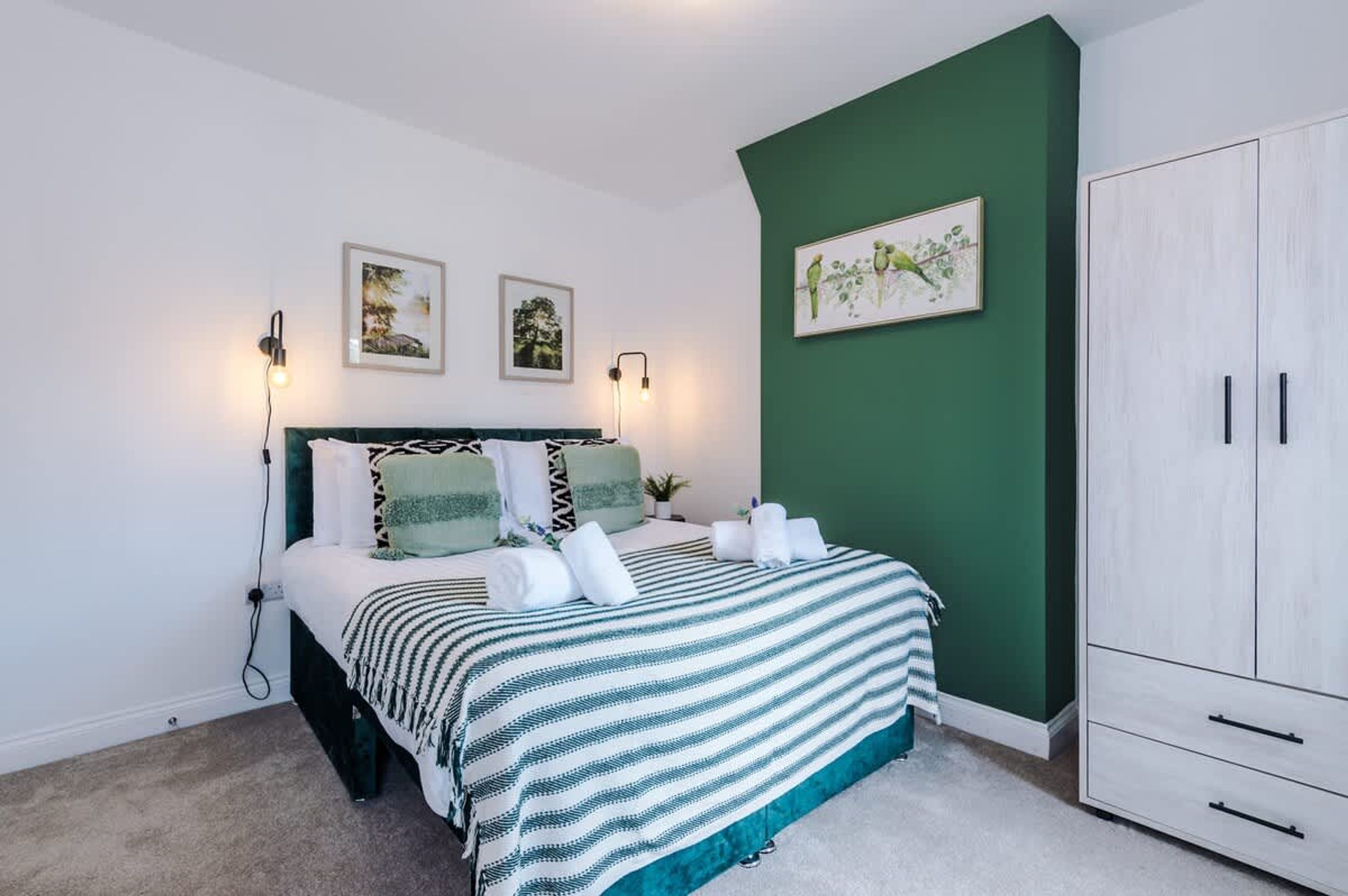 Un dormitorio con una cama, dos luces fijadas a la pared, una pared de acento verde y un armario blanco.