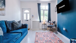A room with a blue sofa, a patterned rug, a TV mounted on the wall, and a window with curtains. - Gorgeous 3-bed Home Amazing Location Sleeps 7 (Nantwich)