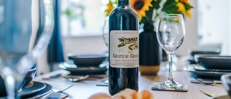 A dining table with a bottle of Chateau Chanteur wine, a glass, and a vase with sunflowers.