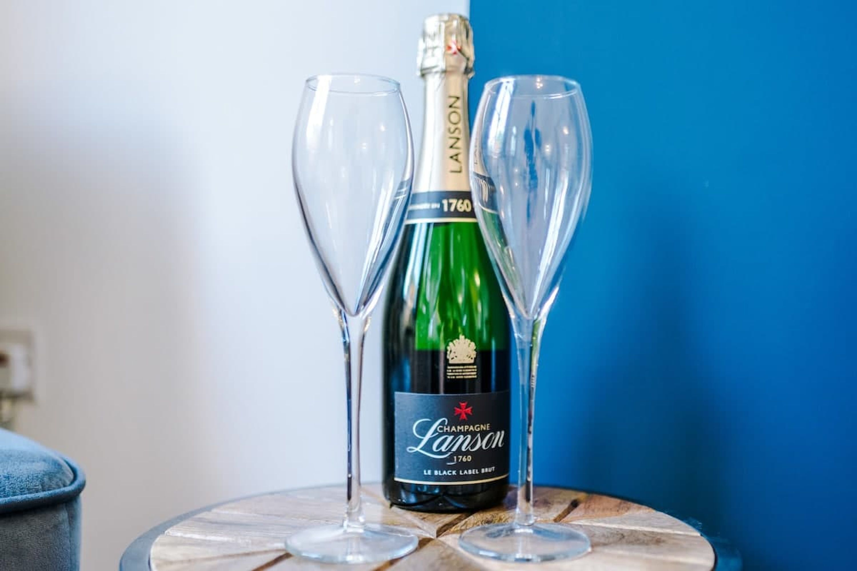 Una ampolla de xampany Lanson 1760 amb dos vasos buits sobre una taula rodona.