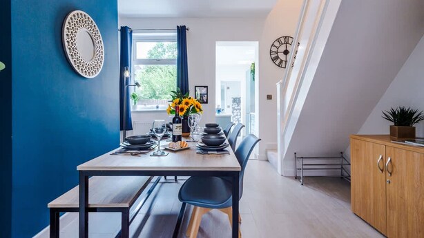 A dining area with a table set for four, a blue wall, a decorative mirror, and a clock on the wall. - Gorgeous 3-bed Home Amazing Location Sleeps 7 (Nantwich)