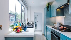 A modern kitchen with teal cabinetry, a large window, and a fruit bowl on the counter. - Gorgeous 3-bed Home Amazing Location Sleeps 7 (Nantwich)