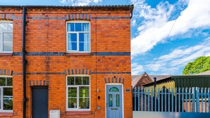 A two-story brick building with a blue door and windows, a visible number '23' on the door, and a fence in the background. - Gorgeous 3-bed Home Amazing Location Sleeps 7 (Nantwich)