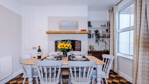 A dining area with a wooden table, white chairs, a vase of sunflowers, and a bookshelf. - NEW Spacious Stylish Home City Centre Sleep 4 (Chester)