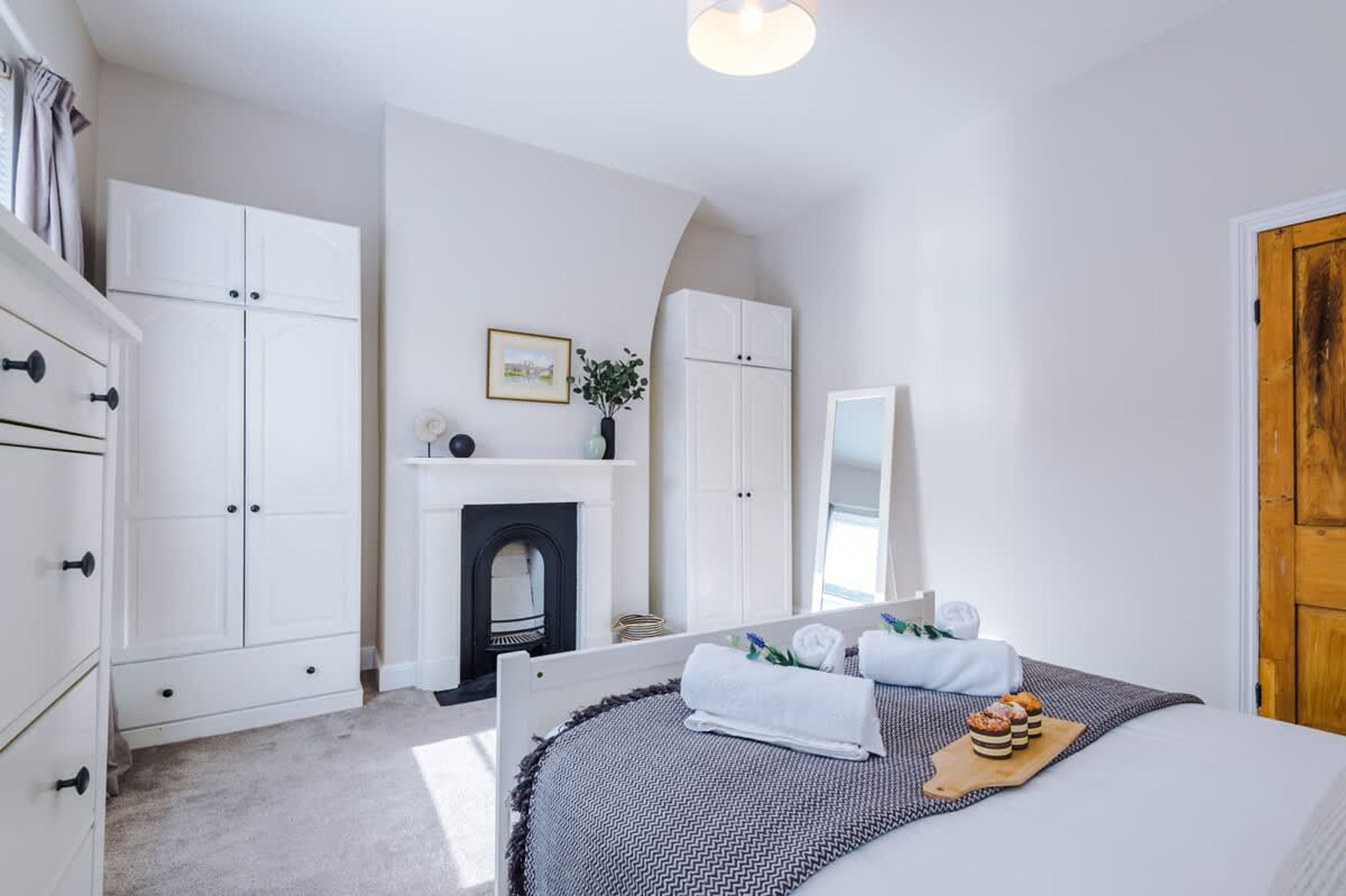 A bedroom with a bed, white wardrobe, fireplace, and a wooden door.