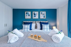 A hotel room with a bed, blue walls, and three framed pictures. - NEW Stylish Apartment Amazing Location Sleeps 6 (Salford)