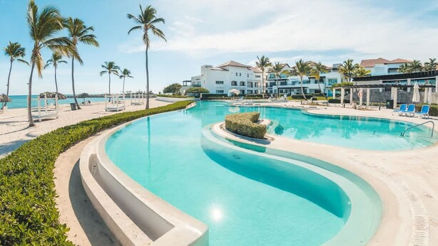 Piscina di un resort con design curvo, palme e vista sulla spiaggia.