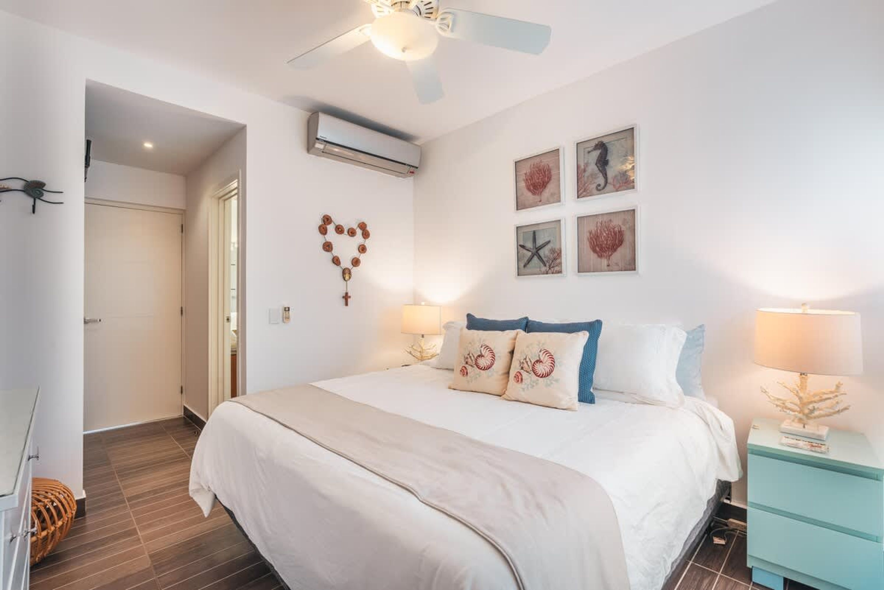 Un dormitorio con cama, lámparas de noche, cuadros en la pared y ventilador de techo.
