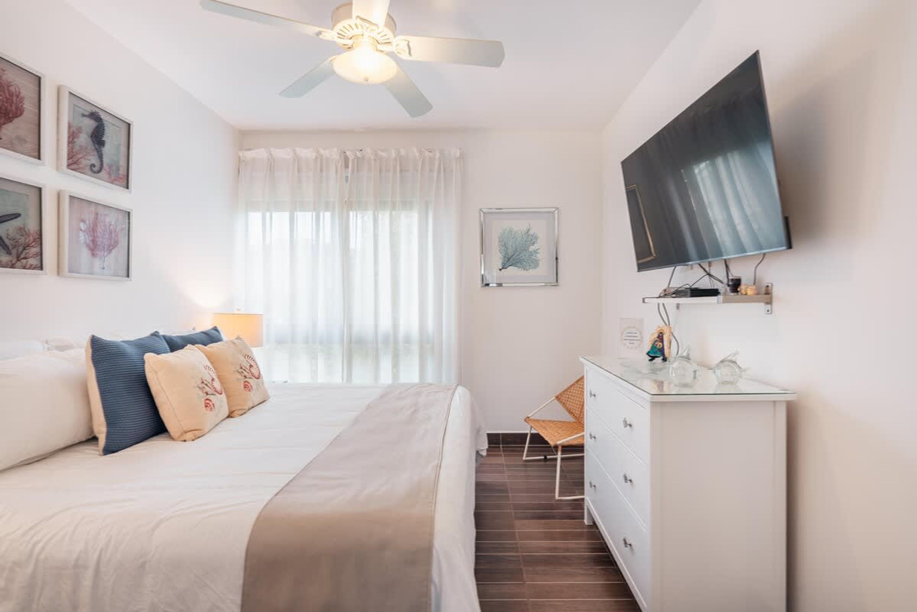 A bedroom with a bed, a dresser, a television, and artwork on the wall.