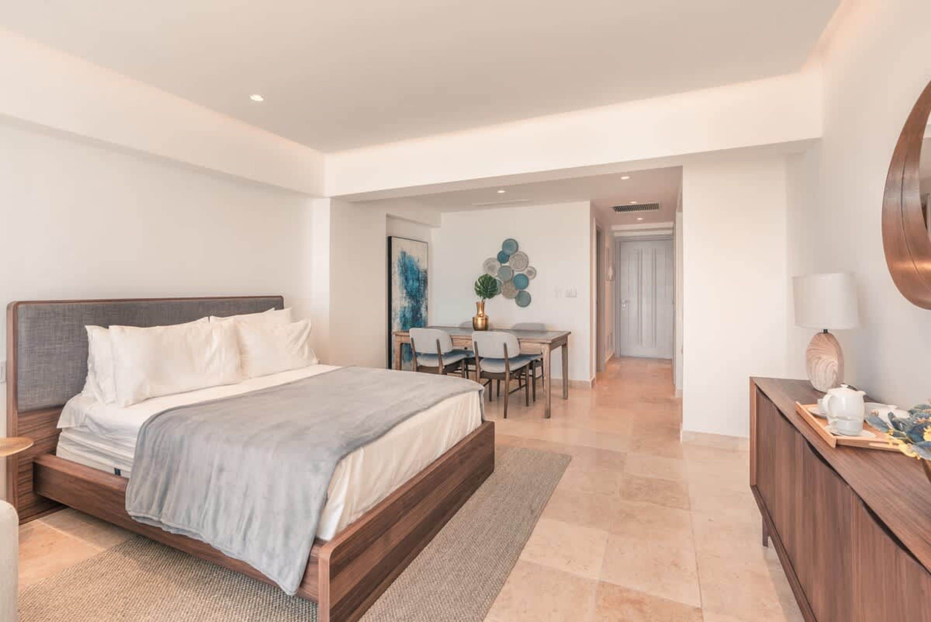 A modern bedroom with a large bed, a desk, and a dining area.