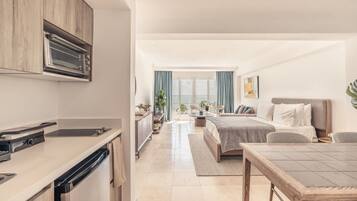 Habitació d'hotel moderna amb cuineta, llit, zona de menjador i vista al mar.