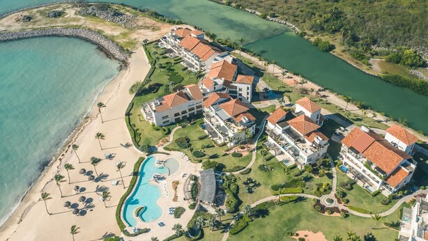 Eine Vogelperspektive zeigt ein Resort mit mehreren Gebäuden, einem Swimmingpool und einem Strand.