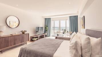A modern hotel room with a bed, a TV, a desk, and a view of the sea.