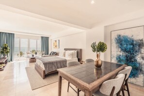 A modern hotel room with a large bed, a dining table, and a view of the sea. - Studio for two w Ocean View at Punta Palmera Gc5 (Punta Cana)