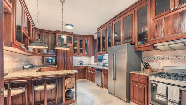 A kitchen with wooden cabinets, a stainless steel refrigerator, a gas stove, and a bar area with stools. - 5br Villa Nearby the Beach w Pool in Casa de Campo (La Romana)