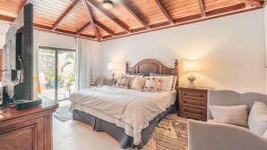 A bedroom with a wooden ceiling, a bed with pillows, a nightstand, a lamp, and a TV on a wooden dresser. - 5br Villa Nearby the Beach w Pool in Casa de Campo (La Romana)