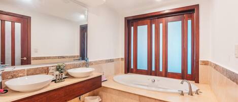 Un baño con dos lavamanos, una bañera, un espejo grande y una puerta de madera.