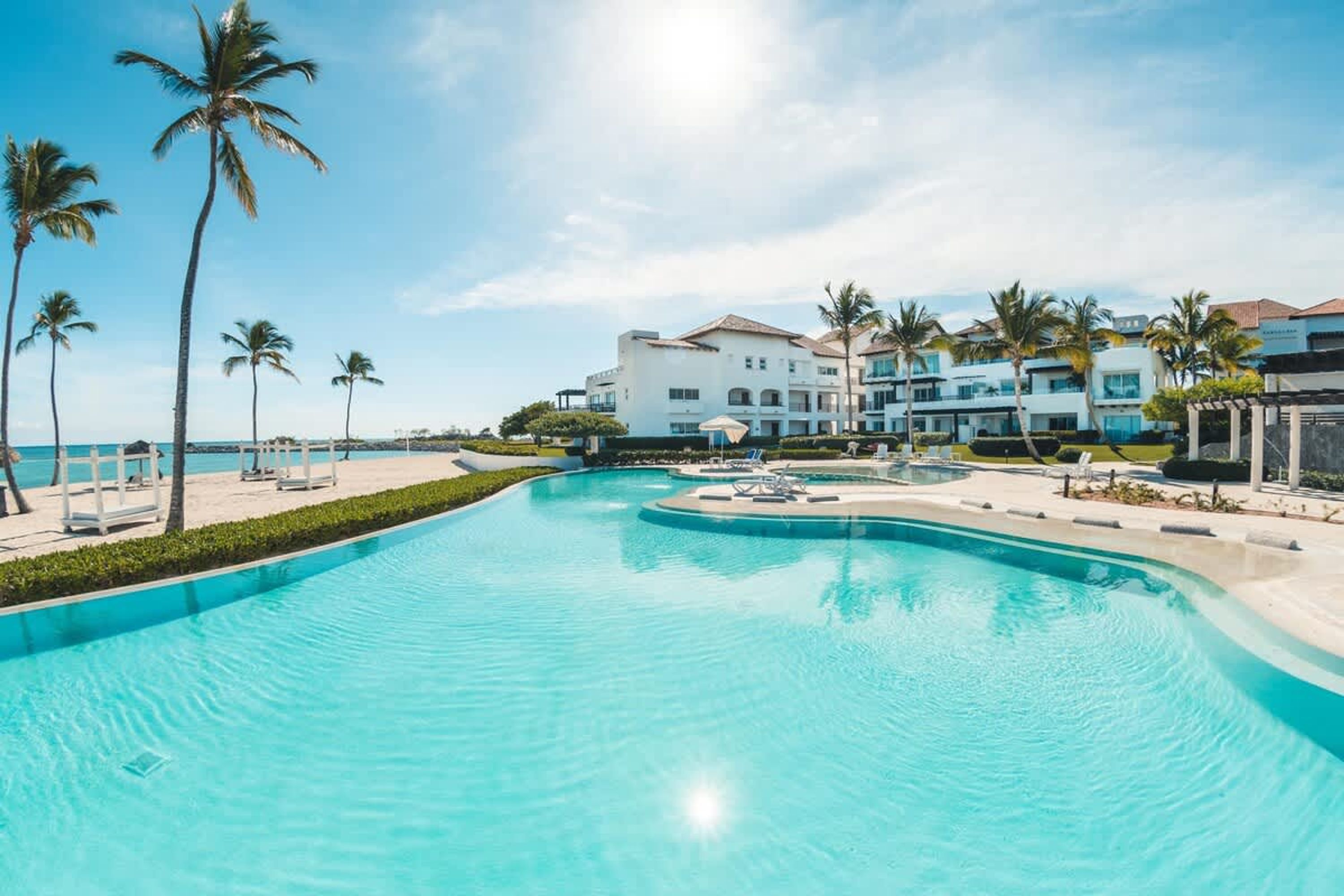A resort with a large swimming pool, palm trees, and beachfront buildings.