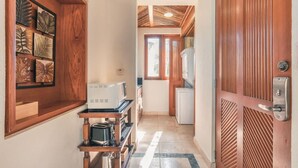 Un couloir étroit avec une porte en bois, un coin cuisine équipé d’appareils électroménagers et un mur orné de motifs décoratifs en forme de feuilles.