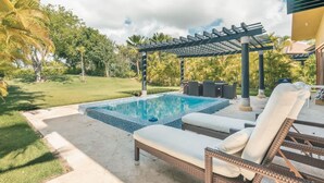 Une piscine avec des chaises longues, une pergola et une pelouse agrémentée d’arbres.