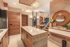 A modern kitchen with wooden cabinets, a marble countertop, and a staircase leading to an upper level. - Apt 3 Bedroom 6 Guests Private Jacuzzi (Punta Cana)