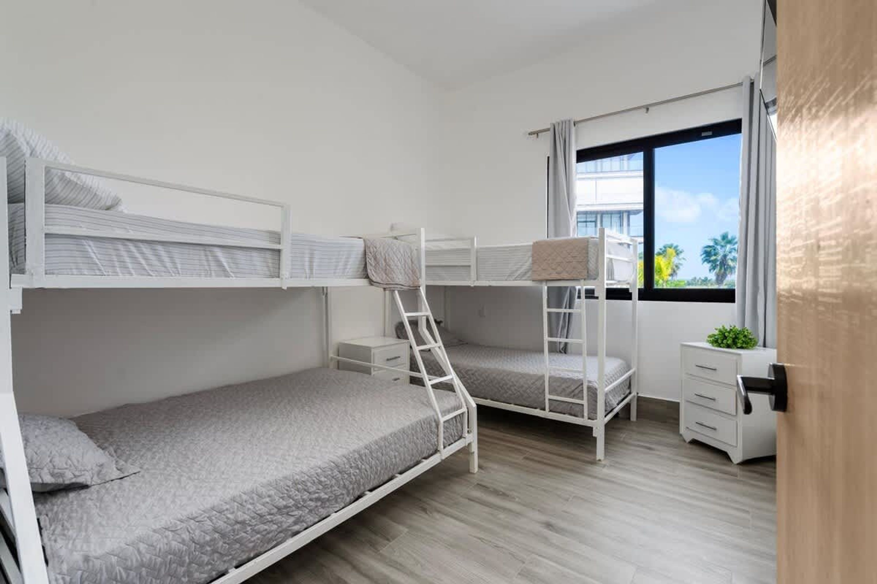 A room with bunk beds, a desk, a chair, and a window with a view of palm trees.