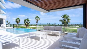 Un espacio exterior moderno con piscina, mobiliario blanco y vistas al océano.