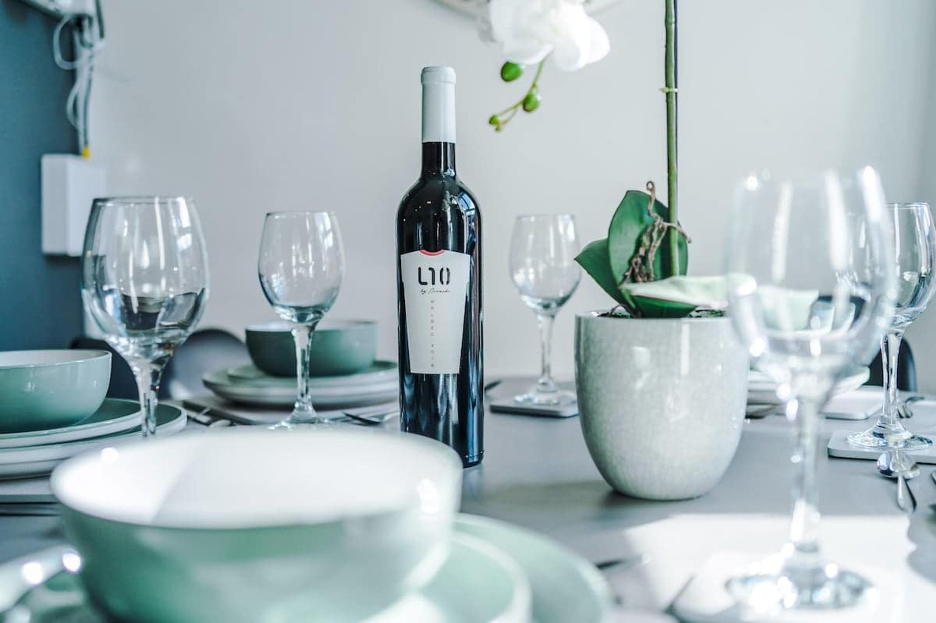 A dining table set with wine glasses, plates, and a bottle of wine.