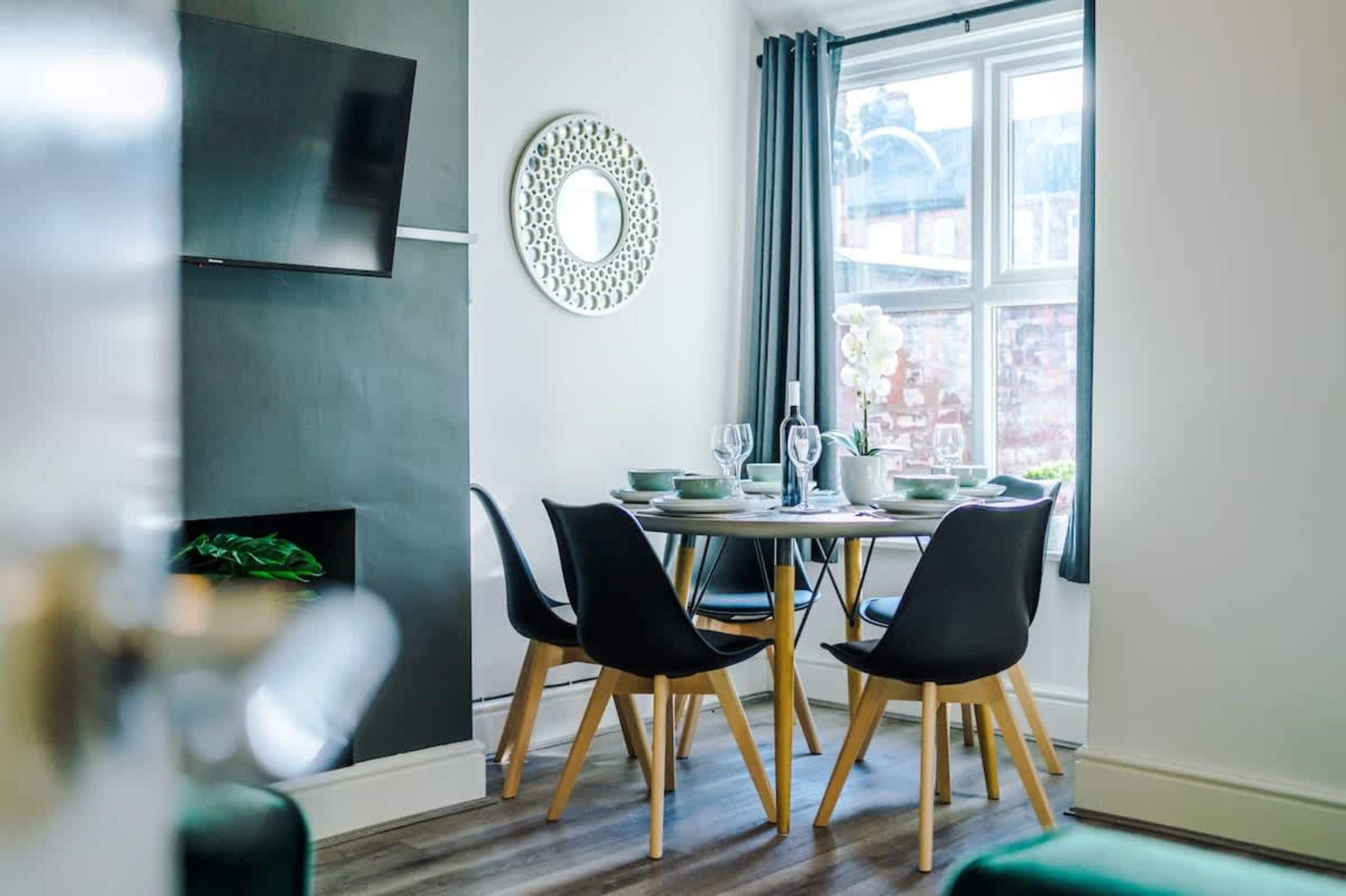A dining area with a table set for four, a flat-screen TV mounted on the wall, and a decorative mirror.