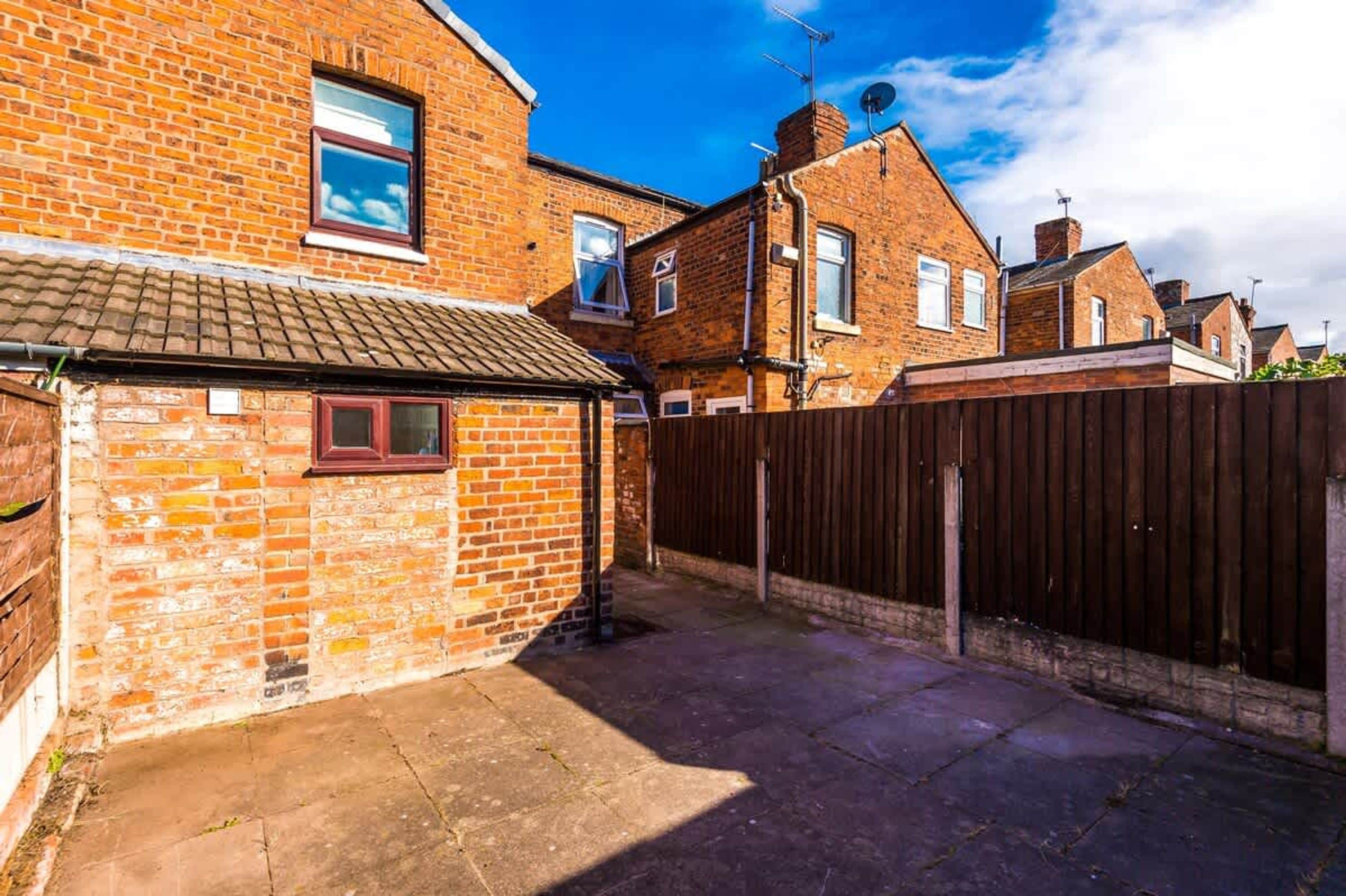 A brick house with a small attached garage, a wooden fence, and a clear blue sky.