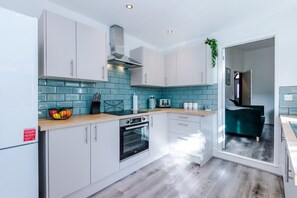 A modern kitchen with white cabinets, a blue tiled backsplash, and a built-in oven. - Modern Home Ideal for Business Groups Sleeps 7 (Crewe)
