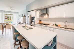 A modern kitchen with white cabinetry, a central island with stools, a gas stove, and a large window overlooking a pool. - Two-bedroom apt With Pool View bbq in Lake View (Las Terrenas)
