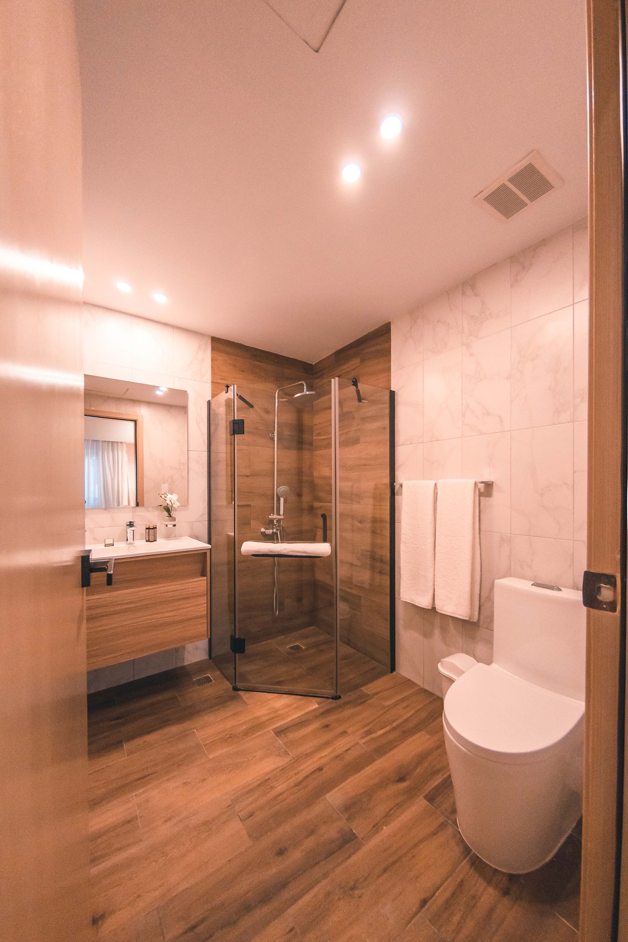 A modern bathroom with a glass-enclosed shower, a wooden vanity, and a white toilet.