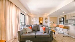 A modern living room with a grey sofa, orange and black patterned cushions, a dining area with a bar, and a kitchen with stainless steel appliances. - Regatta Living 906 (Santo Domingo)