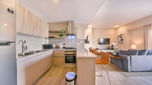 A compact kitchen with modern appliances, a dining area with a sofa and table, and a living room with a TV and decorative items. - Regatta Living 906 (Santo Domingo)