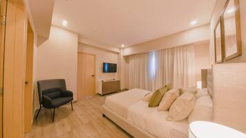 Una habitación de hotel con cama, sillón, televisor y escritorio.