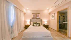 A bedroom with a large bed, two bedside tables with lamps, a headboard, and a shower area. - Regatta Living 906 (Santo Domingo)