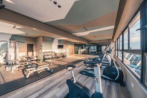 A modern gym with various exercise equipment, large windows, and a view of the city. - Regatta Living 906 (Santo Domingo)