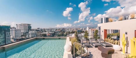 A rooftop pool with clear water, lounge chairs, and a city view.