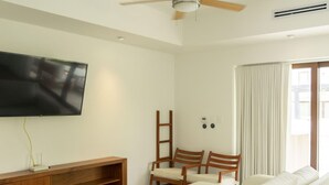 A living room with a sofa, a TV, a ceiling fan, and a window with curtains.