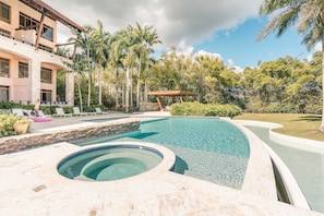 A swimming pool with a stone-lined edge, a lounge area with white chairs, and a building with multiple windows. - 4br Maid Included Golf Course View 8 Guest (La Romana)